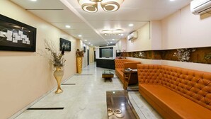 A modern hotel lobby with a long reception desk, a seating area with a tufted orange sofa, and a decorative wall with a floral arrangement. - HOTEL THE SUDESH (Raipur)