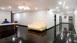 A modern reception area with a receptionist desk, a cream-colored sofa, and a sleek black floor. - HOTEL THE SUDESH (Raipur)