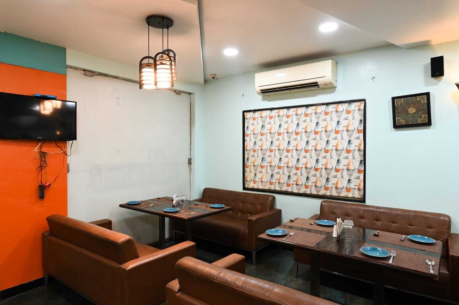 A dining area with brown leather booths and tables, an air conditioning unit, a mounted television, and a patterned wall.