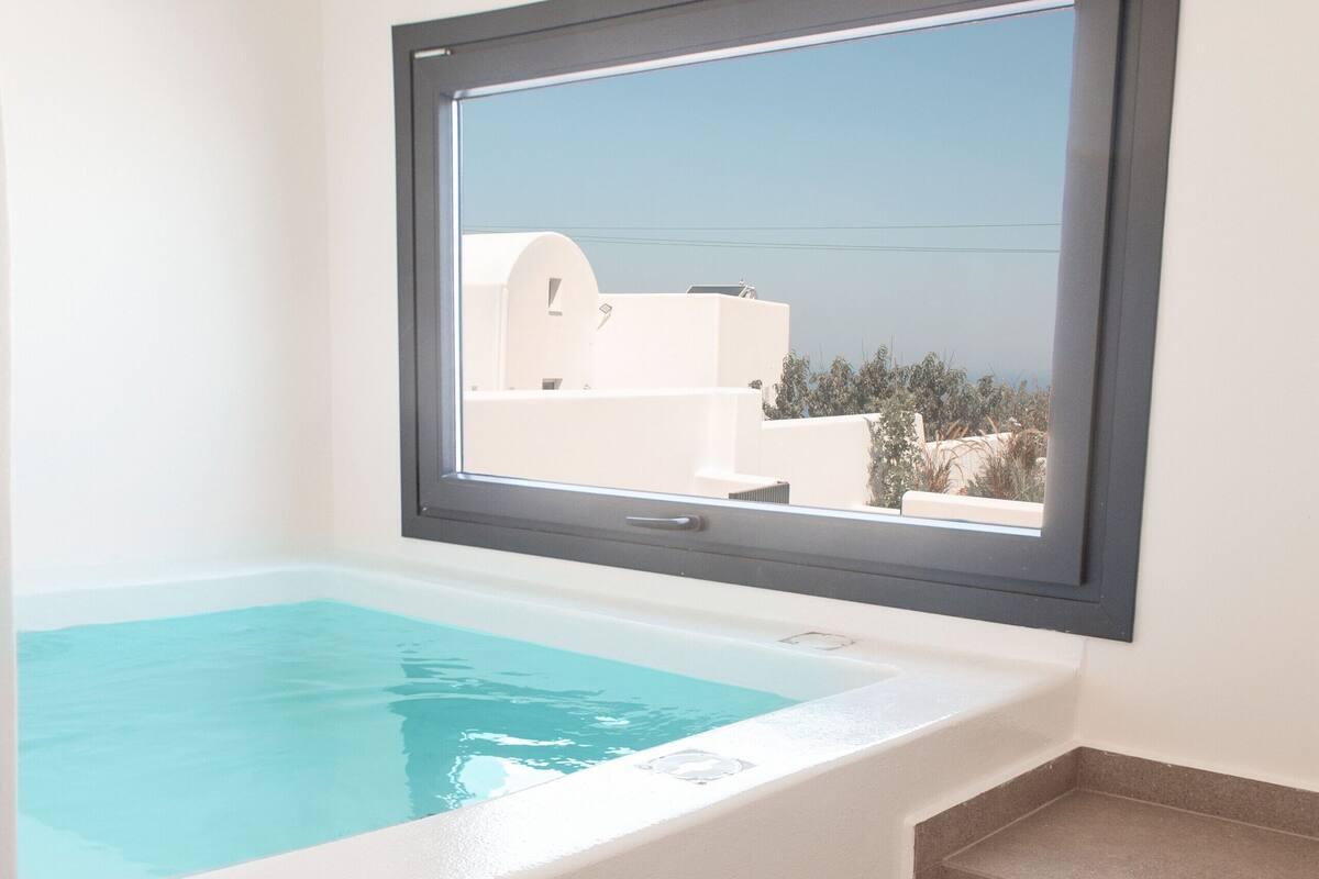 Ein modernes Badezimmer mit einer eingebauten Badewanne, einem Fenster mit Blick auf ein Gebäude und einer kleinen Treppe.