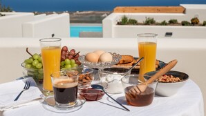Mesa de desayuno con diversos alimentos y bebidas, con vista a una piscina y al océano.