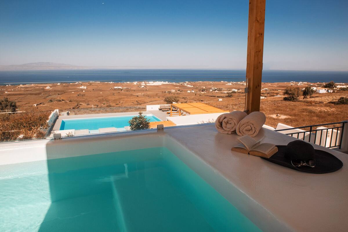 Ein Pool mit Blick auf das Meer und eine Holzterrasse mit Handtüchern und einem Hut.