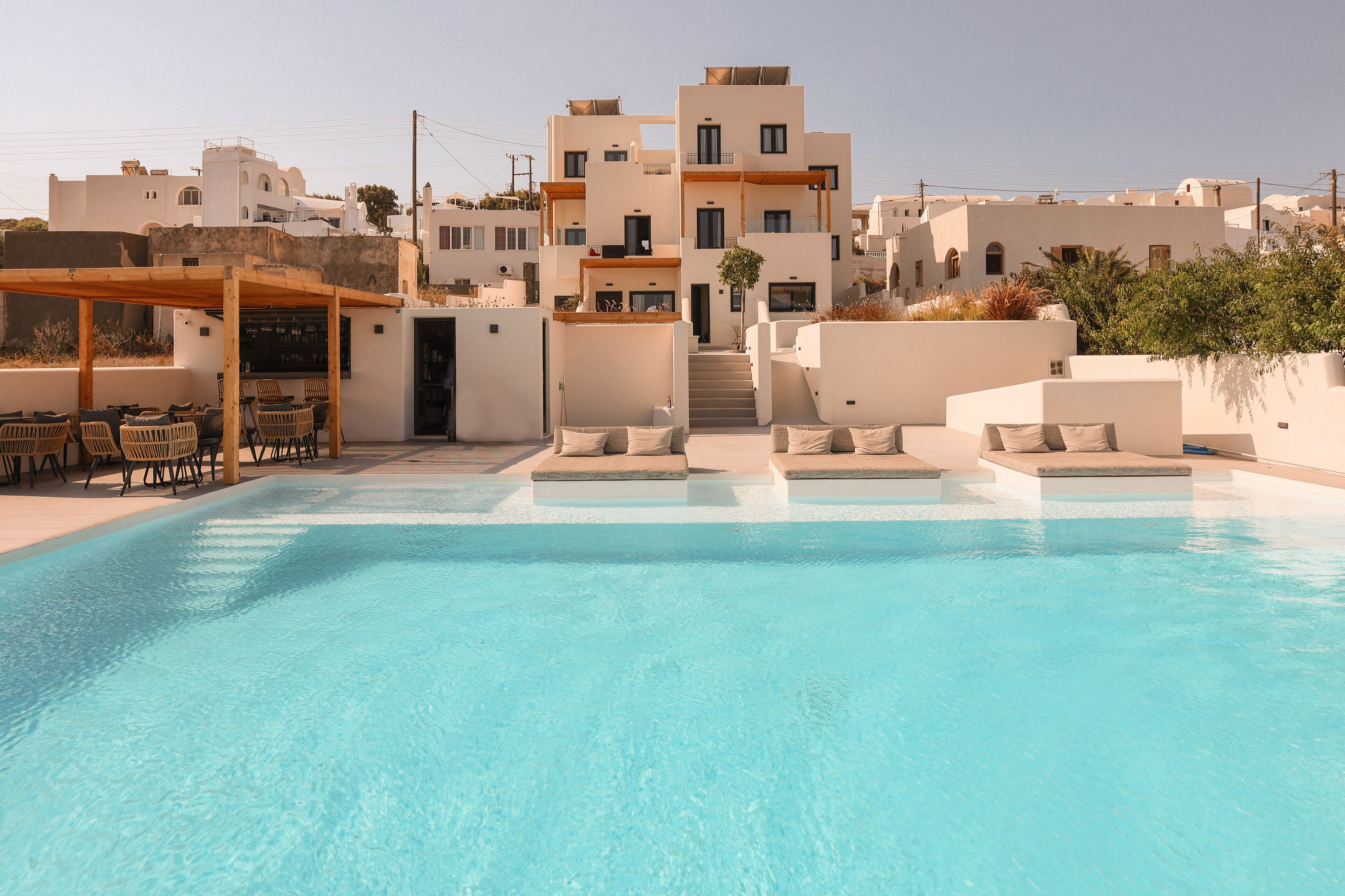 A swimming pool with lounge chairs, a covered seating area, and a staircase leading to a building with multiple balconies.