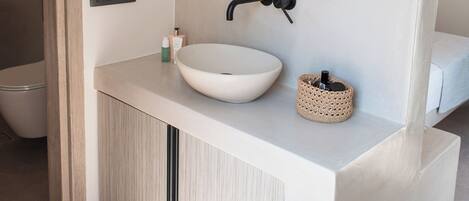 Une salle de bain moderne avec un lavabo blanc, un robinet noir et un miroir rond placé au-dessus.