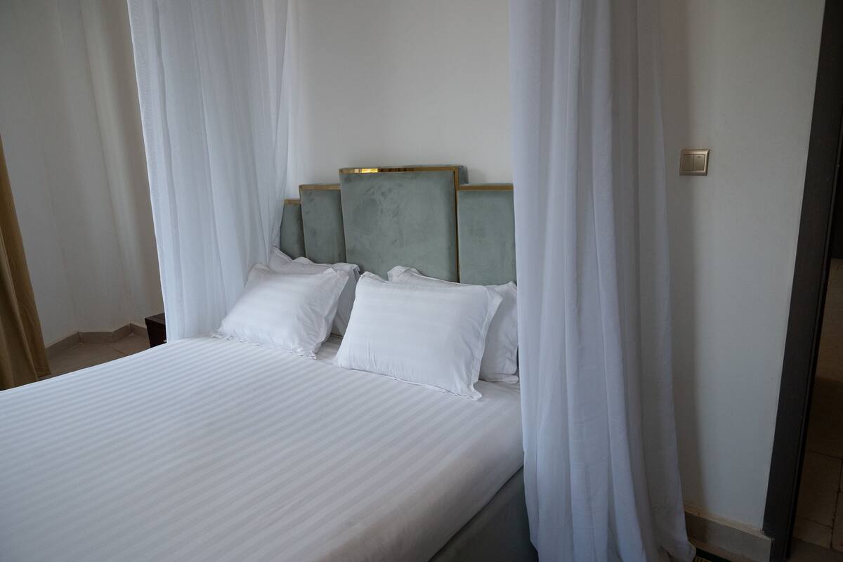 Una cama con ropa de cama blanca y un cabecero con un panel de color claro.