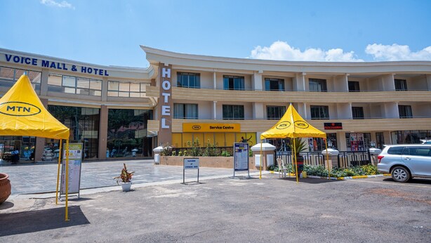 Hotel com centro de atendimento, vários andares e área de estacionamento com toldos amarelos.