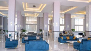 A spacious lobby with blue sofas, a central dining area, and large windows allowing natural light. - The Voice Hotel (Entebbe)