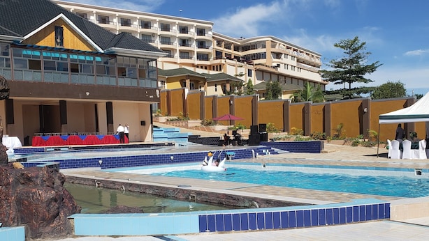 A hotel with a swimming pool, outdoor seating, and a multi-story building with balconies. - The Voice Hotel (Entebbe)