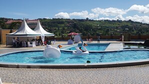 Piscina com boias de cisne decorativas, área de estar coberta e vista para uma paisagem montanhosa ao fundo.