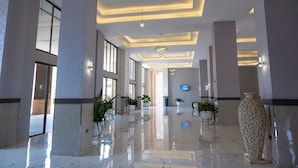 A spacious lobby with a polished marble floor, large columns, and potted plants. - The Voice Hotel (Entebbe)