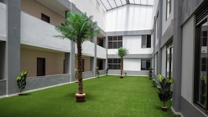 A courtyard with artificial grass, potted plants, and a modern building facade. - The Voice Hotel (Entebbe)