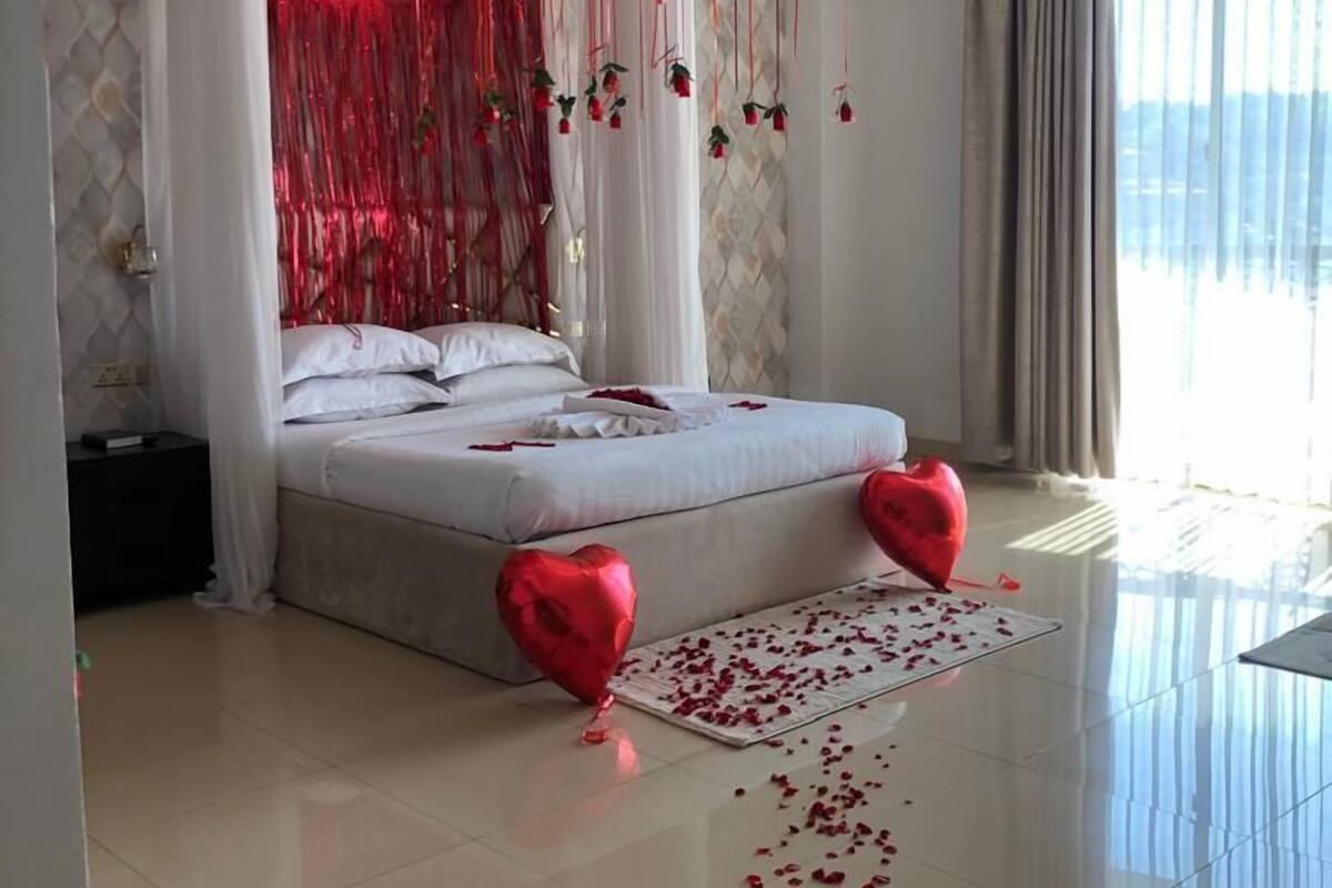 Un dormitorio moderno con una cama grande, cortinas translúcidas y un arreglo de globos rojos.
