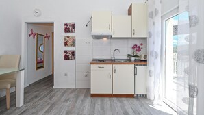 A compact kitchen with white cabinets, a sink, and a stove. There are floral wall art pieces and a butterfly decoration on the wall. - 1 bedroom gorgeous apartment in Okrug Gornji (Okrug Gornji)