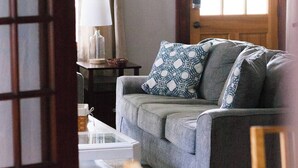 A living room with a sofa, a coffee table, and a wooden chair. A door with a window is visible in the background. - Bring everyone. Spread out, settle in, and make Montgomery feel a little more like home. (Montgomery)