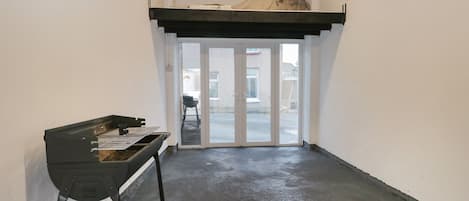 A narrow hallway with a black metal table and a bench, leading to a glass door with a view of the outside.