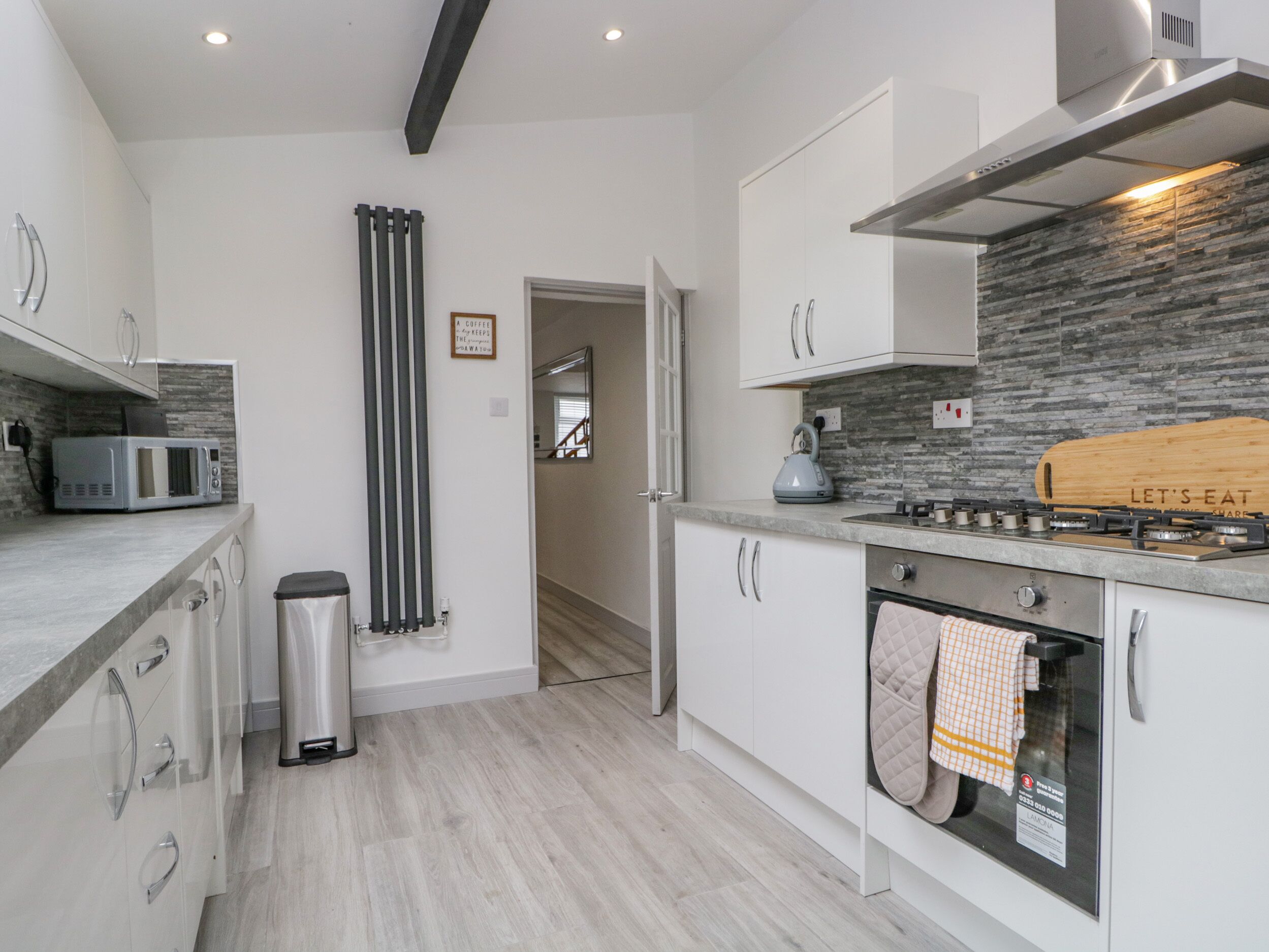 A modern kitchen with white cabinets, a microwave, a kettle, and a stove.