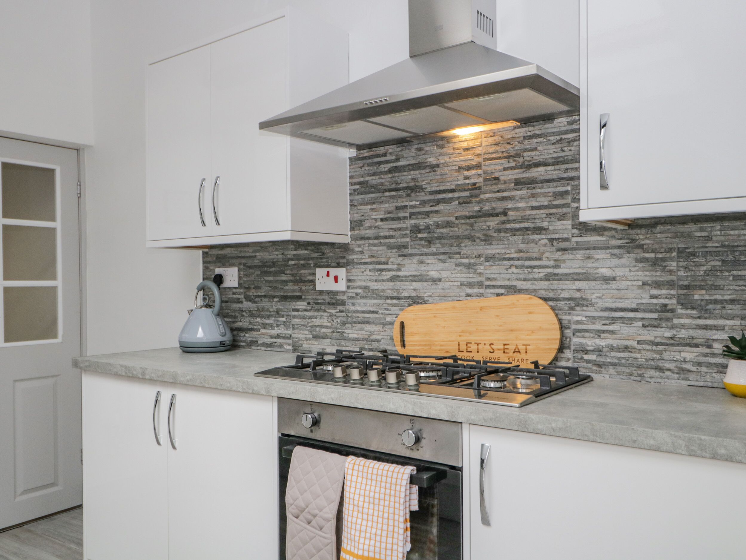 Una cocina moderna con armarios blancos, protector contra salpicaduras de piedra, estufa a gas y horno empotrado.