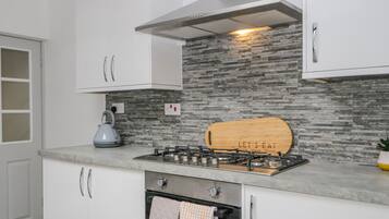 Una cocina moderna con armarios blancos, protector contra salpicaduras de piedra, estufa a gas y horno empotrado.