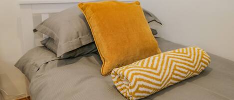 Una cama con un edredón gris y dos almohadas, una de color liso y la otra con estampado de rombos.