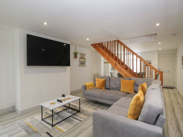 Una sala de estar moderna con un sofá gris, cojines amarillos, una mesa de centro blanca y una escalera de madera.