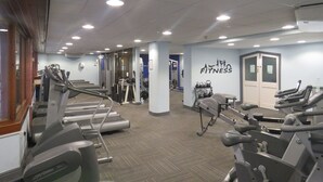 Une salle de sport équipée de tapis de course, d’appareils de musculation et d’une enseigne murale indiquant « FITNESS ».