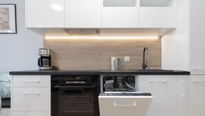 A modern kitchen with white cabinetry, a built-in dishwasher, a coffee maker, and a kettle. - Comfortable Apartment | Jacuzzi, Sauna and Gym in the Building (Miedzywodzie)