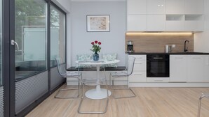 A modern kitchen with white cabinets, a black countertop, and a round dining table with chairs. There is a vase with red flowers on the table. - Comfortable Apartment | Jacuzzi, Sauna and Gym in the Building (Miedzywodzie)