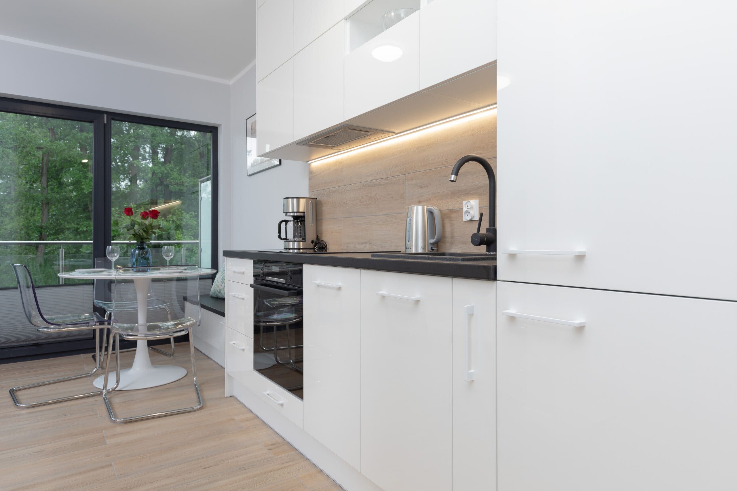 A modern kitchen with white cabinets, a black countertop, and a glass dining table with chairs.