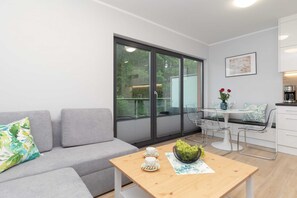 Ein modernes Wohnzimmer mit einem grauen Sofa, einem Holztisch mit einer Vase und Trauben, sowie einem Essbereich mit einem weißen Tisch und Stühlen.