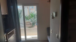 A room with a sliding glass door leading to a balcony, a small seating area, and a door with a keypad lock. - Studio Residence LES DUNES Kantaoui Sousse  (Hammam Sousse)