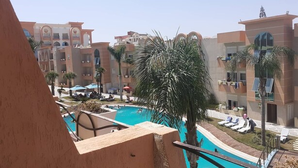 A hotel with a swimming pool, palm trees, and a view of other buildings. - Studio Residence LES DUNES Kantaoui Sousse  (Hammam Sousse)