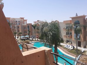 A hotel with a swimming pool, palm trees, and a view of other buildings. - Studio Residence LES DUNES Kantaoui Sousse  (Hammam Sousse)