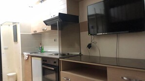 A compact kitchen with a built-in oven, a dishwasher, a sink, and a flat-screen TV mounted on the wall. - Studio Residence LES DUNES Kantaoui Sousse  (Hammam Sousse)