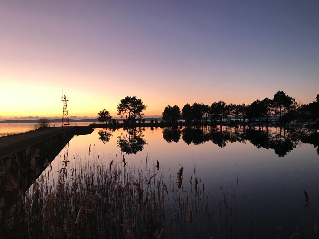 A calm lake at sunset with a bridge and trees in the background.