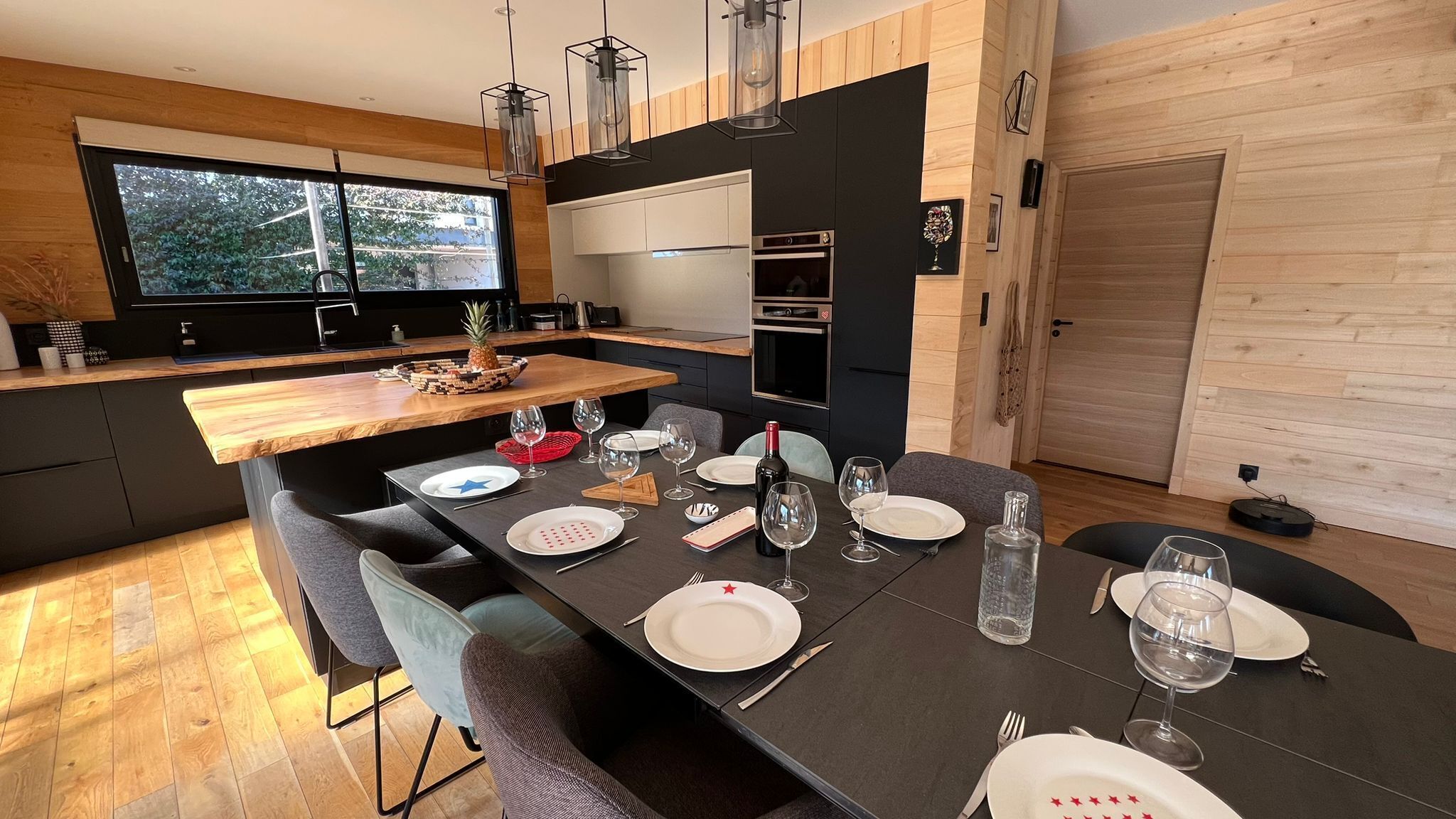 A modern kitchen with a large island, wooden flooring, and a dining area set for six.