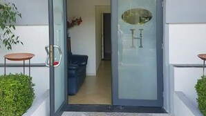 A hotel entrance with a glass door, a sign above the door, and a small table and chair outside. - le pinède vistamare (Pozzuoli)