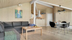 En moderne stue med en grå sofa, et træbord og et spiseområde med et hvidt bord og sorte stole.