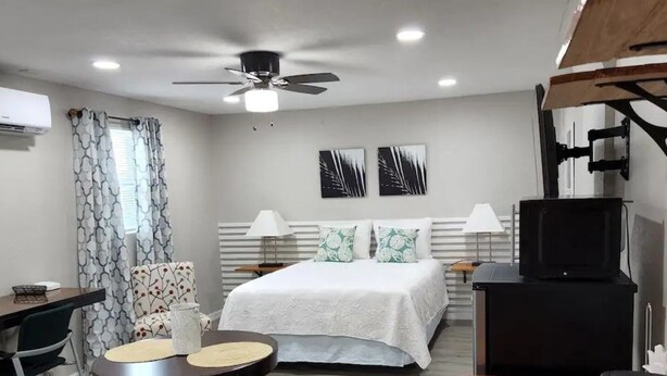 A hotel room with a bed, a desk, a chair, a television, and a ceiling fan. - #28 Little Belleview by Joyful Moments Vacation (Port Richey)