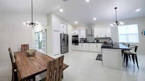 A modern kitchen with white cabinets, a central island, and a dining area with a wooden table and chairs.