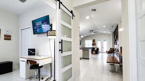 A modern kitchen with a dining area, a TV mounted on the wall, and a sliding glass door leading to a living space.