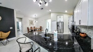 A modern kitchen with a marble countertop, stainless steel appliances, and a dining area with a wooden table and chairs.
