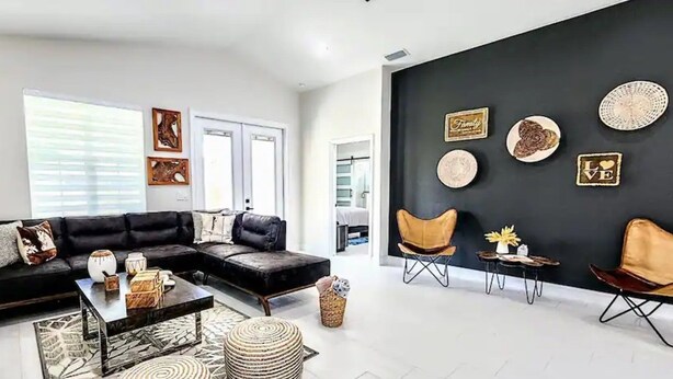 A modern living room with a black sectional sofa, a coffee table, and a black wall with decorative plates and a television mounted above.