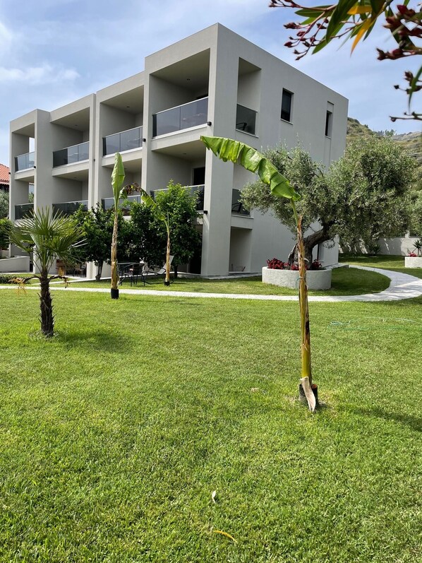 A modern multi-story building with balconies, surrounded by well-maintained grass and a few trees.