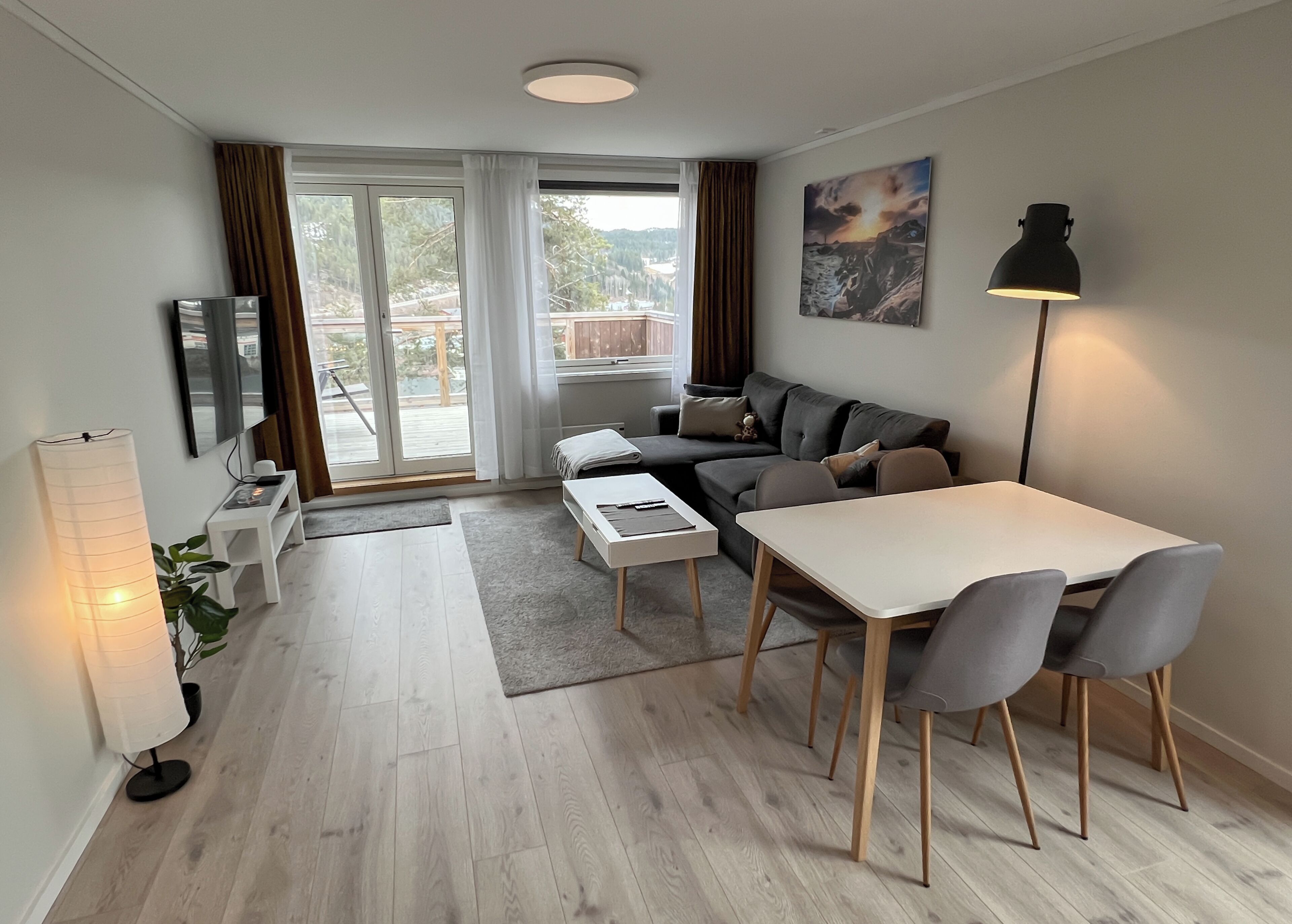 A modern living room with a sofa, dining table, and chairs, a TV, and a painting on the wall.
