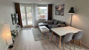 A modern living room with a sofa, dining table, and chairs, a TV, and a painting on the wall.
