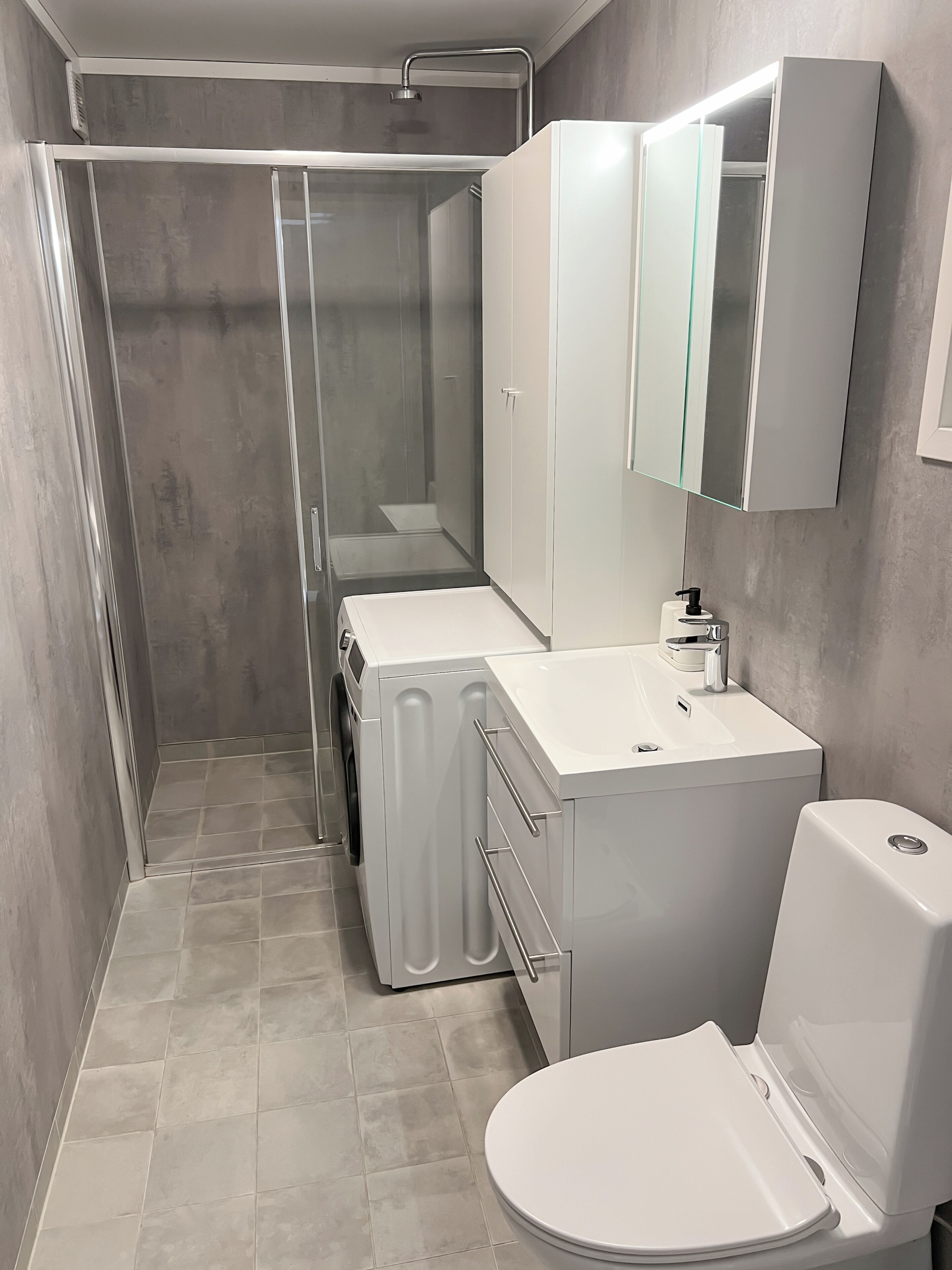 Un baño moderno con ducha de vidrio, un lavamanos blanco y un inodoro.
