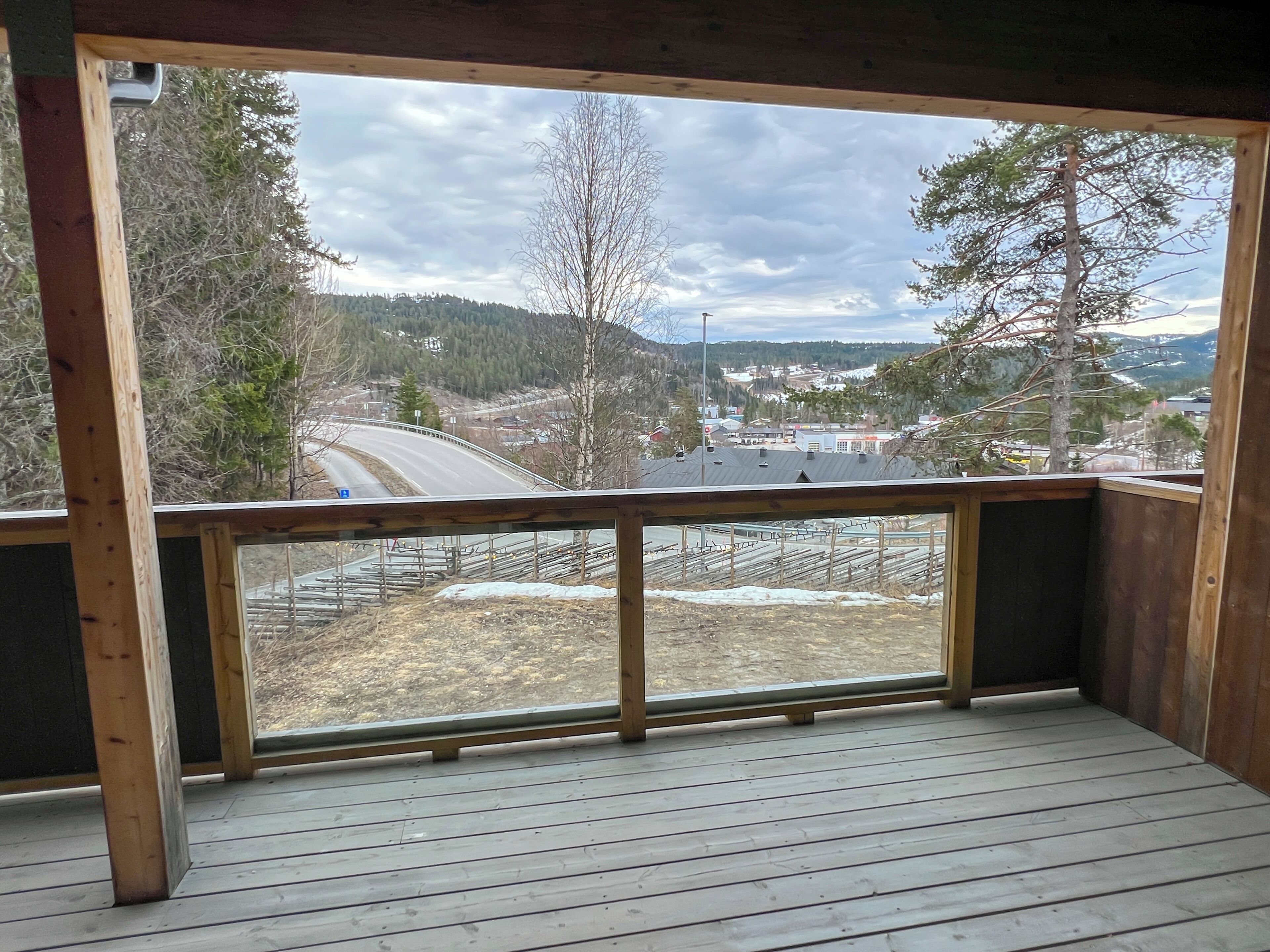 Eine Holzterrasse mit Blick auf eine Straße, Bäume und Gebäude in der Ferne.