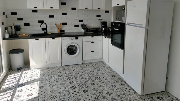 A modern kitchen with white cabinets, a black countertop, a built-in washing machine, and a refrigerator. - Detached house near SAINT MALO (Miniac-Morvan)