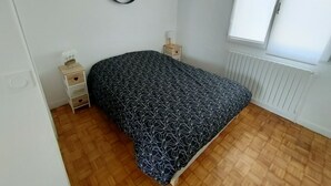 A bedroom with a bed, a bedside table, a nightstand, a radiator, and a window. - Detached house near SAINT MALO (Miniac-Morvan)