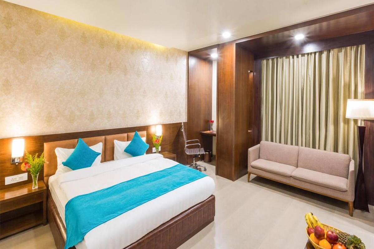 A hotel room with a large bed, a sofa, a nightstand with a lamp, and a fruit basket.